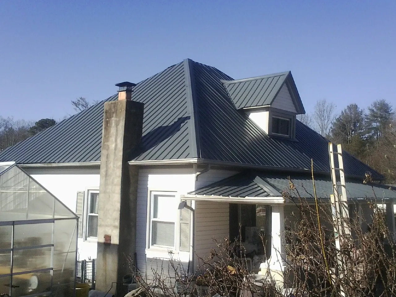 Dark blue standing seam metal roof on a white farmhouse with dormer — Slate & Tile Roof Repair by Roofing Brothers in North Chelmsford
