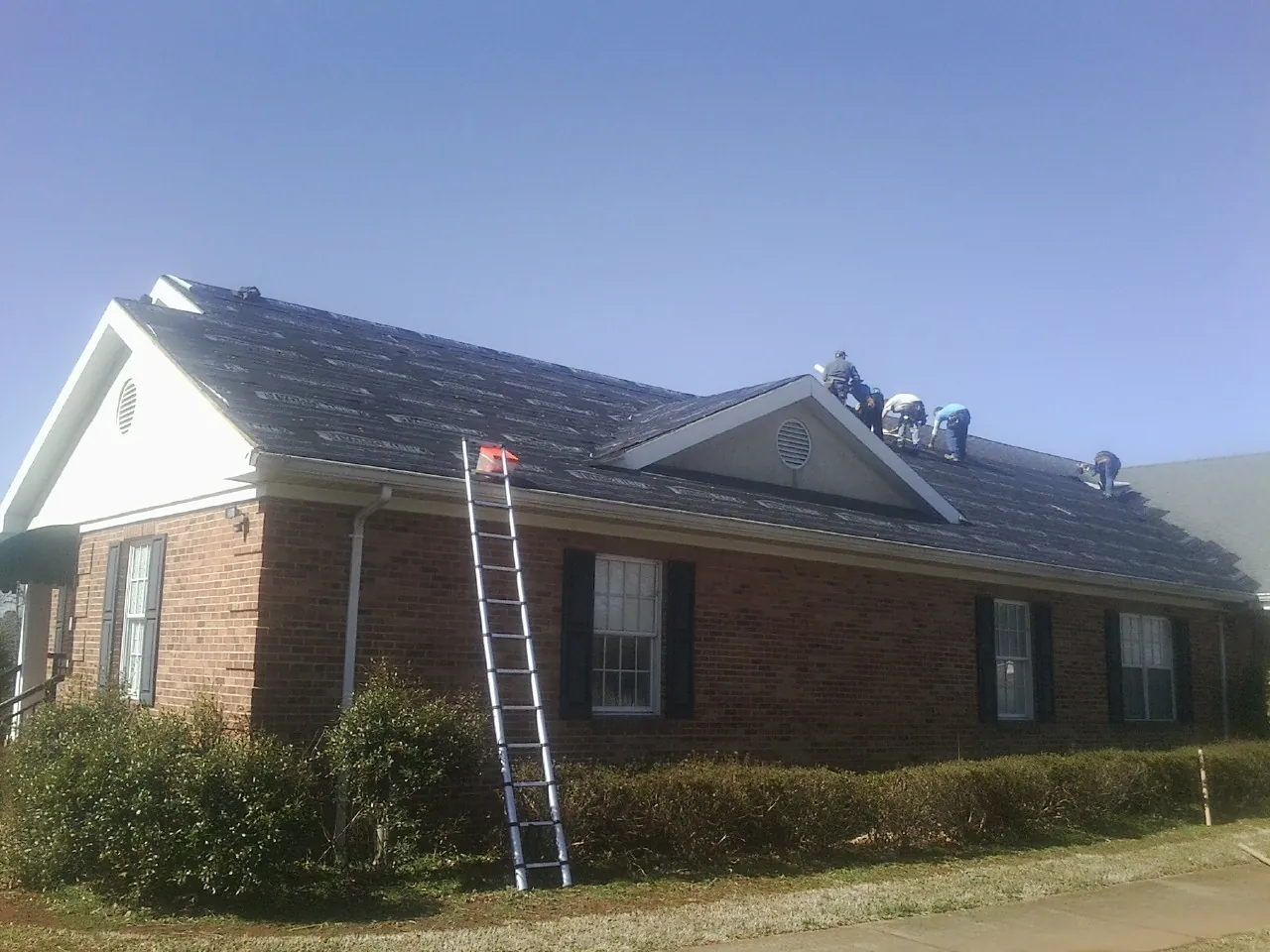 Crew tearing shingles off a brick ranch roof with a ladder set — Emergency Roof Repair work by our crew in North Chelmsford