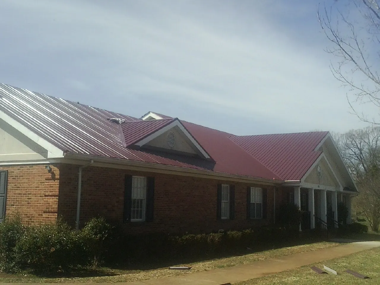 Red metal roof with gabled entries on a long brick building, from a Hail Damage Roof Repair job in North Chelmsford
