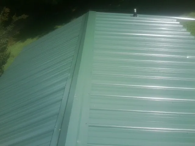 New green metal panels meeting at the ridge of a roof — Flat Roof Repair work by our crew in North Chelmsford