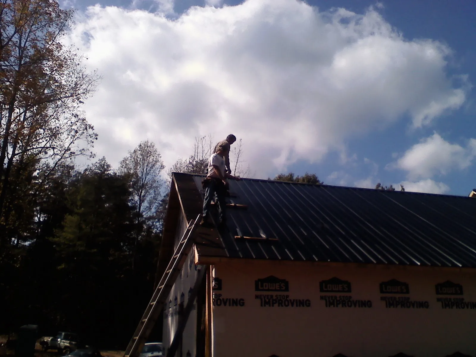 Roofer fastening dark metal panels high against a cloudy sky, from a Roof Inspection job in North Chelmsford