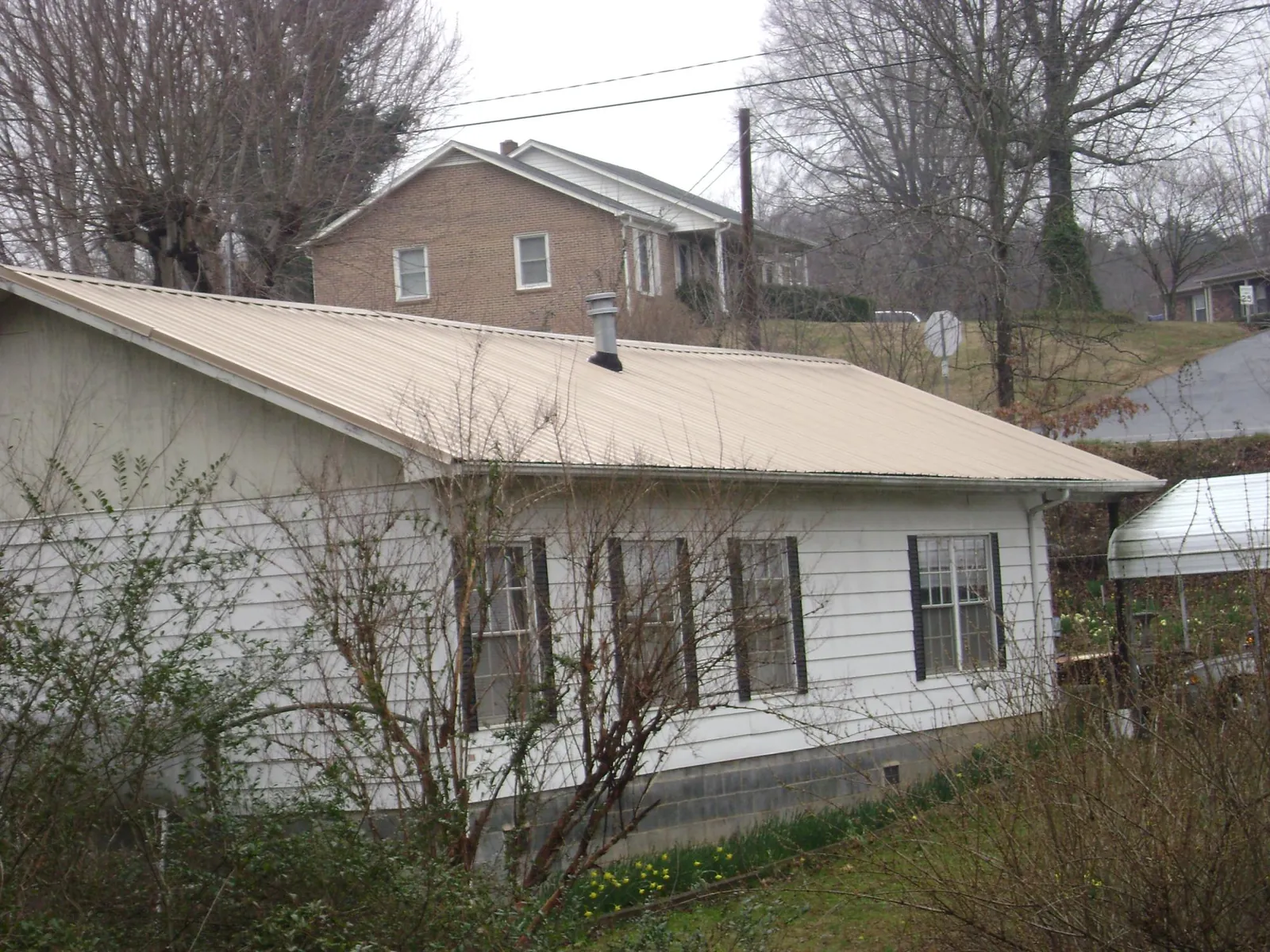 Tan metal roof on a white sided house set into a hillside — Commercial Roofing by Roofing Brothers in North Chelmsford